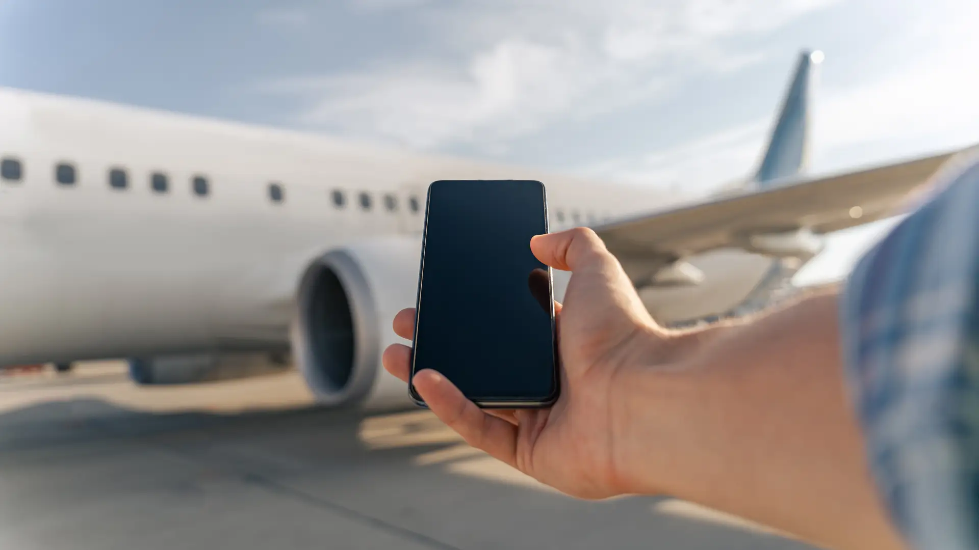 Hand holding a mobile in front of a plane representing Sky roaming